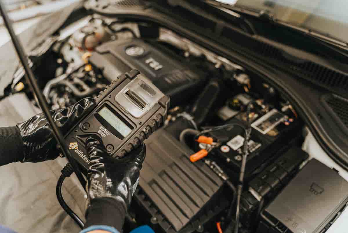 Mechanic testing a car battery with a multimeter under an open hood